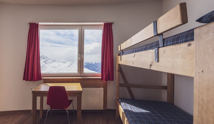 Zimmer mit Stockbett, Kleiderablage, Lavabo und Schreibtisch mit Stuhl | © Davos Klosters Mountains 